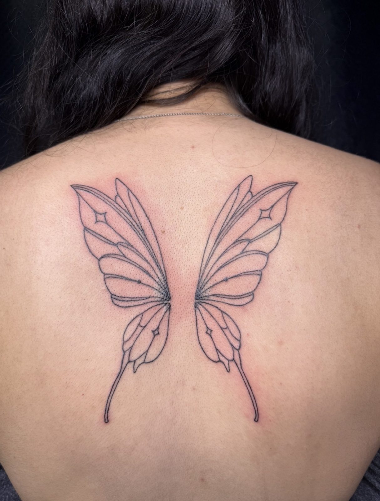 Fine line butterfly wings with sparkle accents across the upper back