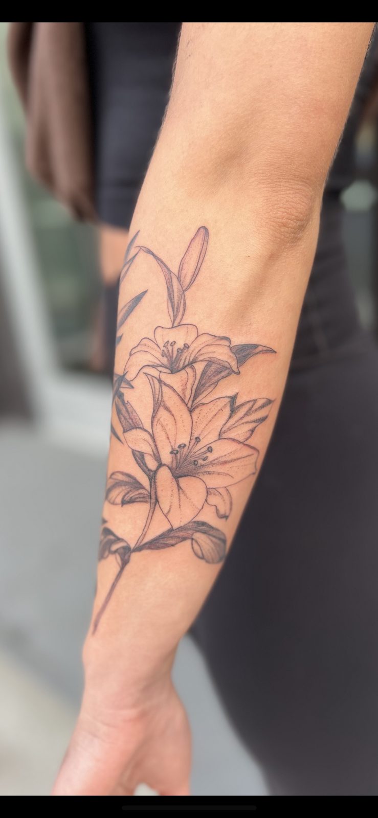 Fine-line lilies tattoo on a forearm by Maddy
